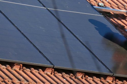 Zwei Handwerker installieren eine Solaranlage auf einem Hausdach. Die Handwerker tragen Bereufskleidung und Helme zur Sicherheit.